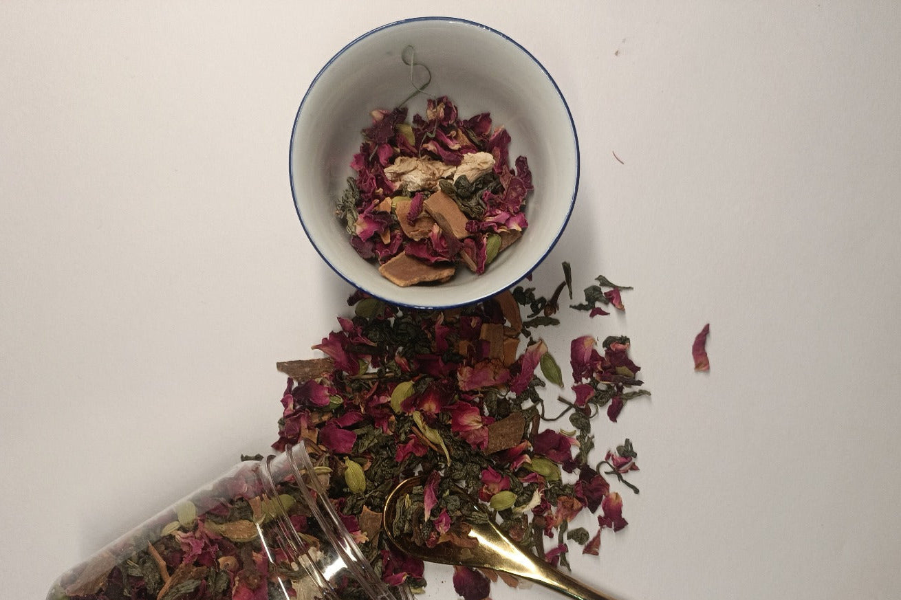 A glass jar with Kashmiri Kehwa mix next to it, with spices like cinnamon, cardamom, and cloves scattered around, indicating the ingredients of the mix.